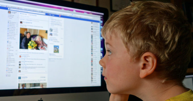 Child children boy looking at Facebook on home computer social media Uk